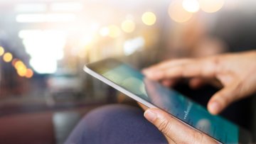 Close up von zwei Händen, die ein Tablet halten, dessen Bildschirm undeutlich sichtbar ist.