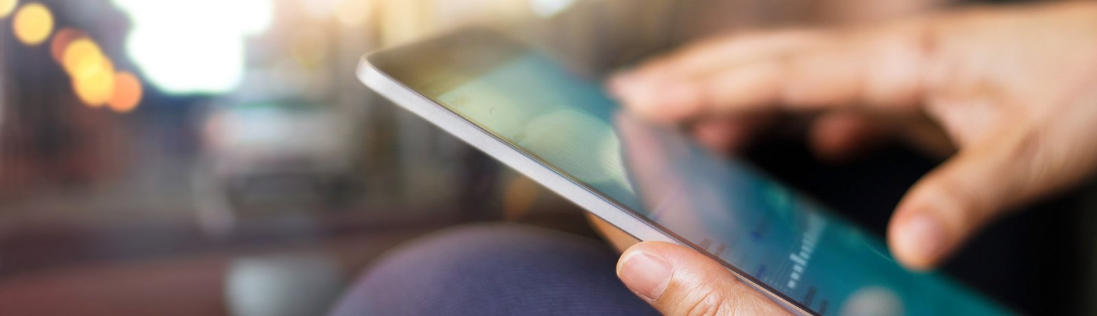 Close up von zwei Händen, die ein Tablet halten, dessen Bildschirm undeutlich sichtbar ist.